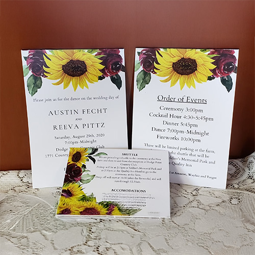 Wedding invitation suite displayed on a lace surface, featuring sunflower floral designs on multiple cards including the invitation, order of events, and accommodations card.